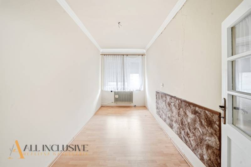 Keskeny szoba fa dekor padlóval, függönyös ablak, radiátor.