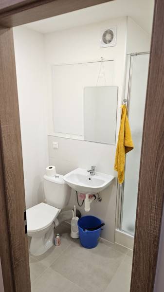 Fürdőszoba a garzonlakásban mosdóval, WC-vel, zuhanyzóval és tükörrel, semleges színekben.