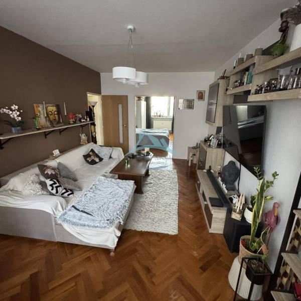 Nappali kanapéval, asztallal és fa dekorációjú padlóval egy háromszobás lakásban.