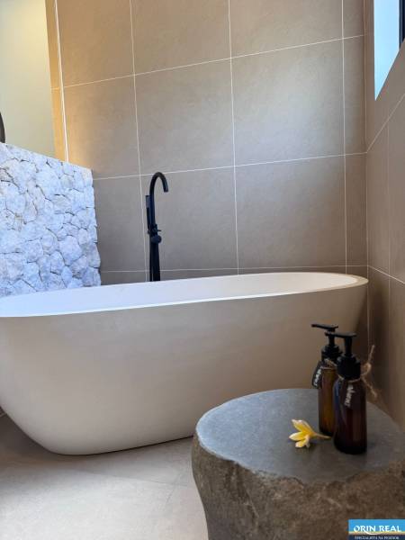 Fürdőszoba családi házban káddal, kővel burkolt fallal és dekoratív üvegcsékkel.