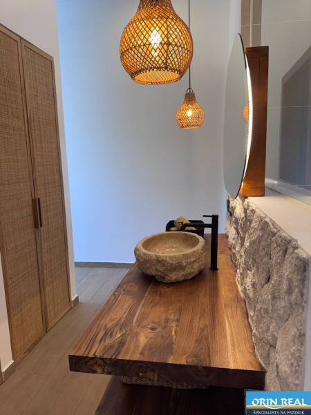 Családi ház belső tere kő mosdóval, fa munkalappal és függőlámpákkal.