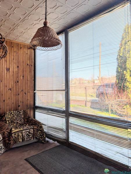 Családi ház rattan lámpával, takaróval borított székkel és redőnyös ablakokkal.