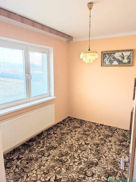 Egy családi házban van egy szoba szőnyegpadlóval, függőlámpával és festménnyel.