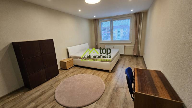 Világos szoba egy kétszobás lakásban ággyal és bútorokkal, fa dekorációjú padlóval.