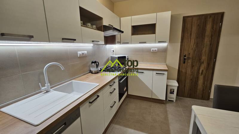 Konyha egy kétszobás lakásban fehér szekrényekkel és fa dekor padlóval.