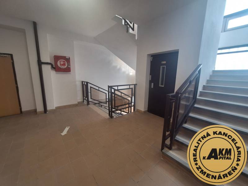 Lépcsőház irodákban csempével és lifttel. A falon vészdoboz.