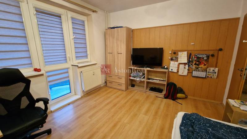 Szoba egy háromszobás lakásban, fa dekorációjú padlóval, televízióval és székkel.