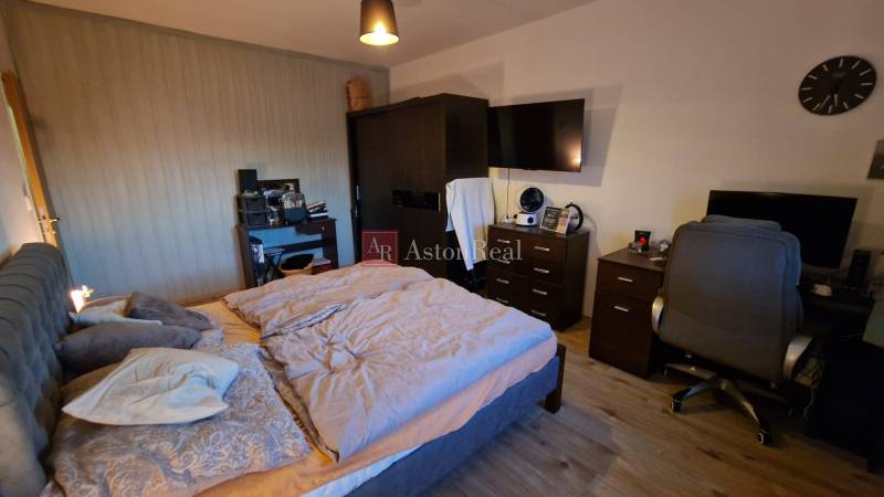 Hálószoba egy háromszobás lakásban, kényelmes ággyal, íróasztallal és fa dekorációjú padlóval.