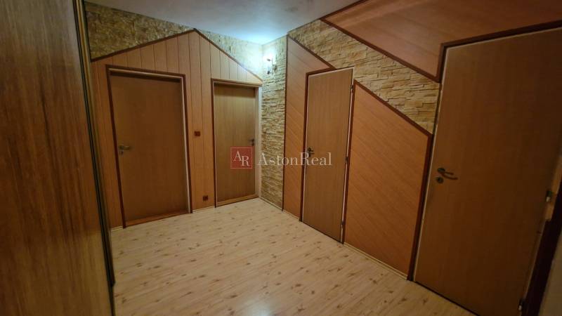 Folyosó három ajtóval és fa dekorációjú padlóval egy háromszobás lakásban.