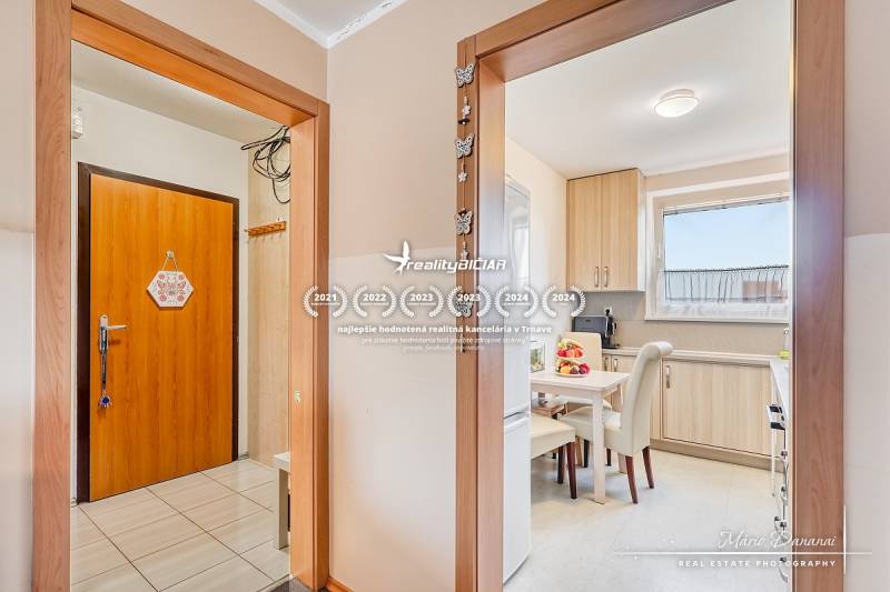 Egy 4 szobás lakás belső tere fa mintázatú padlóval és világos konyhával.