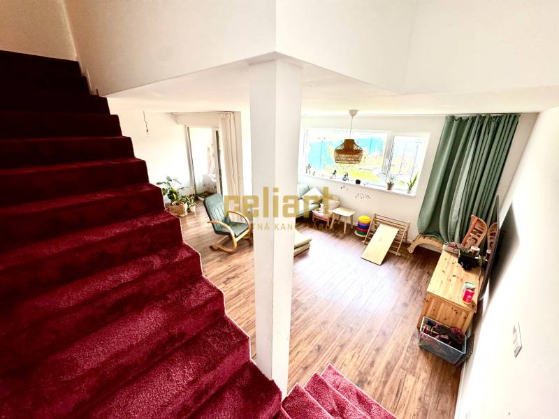 Családi ház belső tere lépcsőházzal és nappalival, fa mintázatú padlóval.