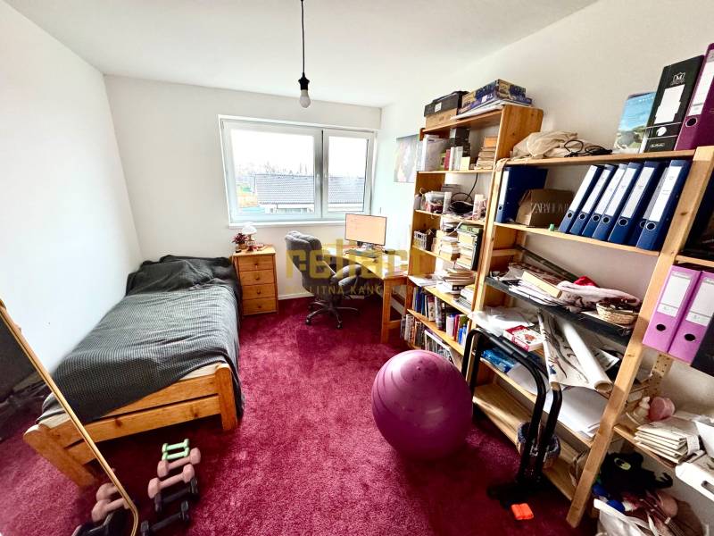 Egy szoba családi házban asztallal, ággyal, polcokkal és piros szőnyeggel.