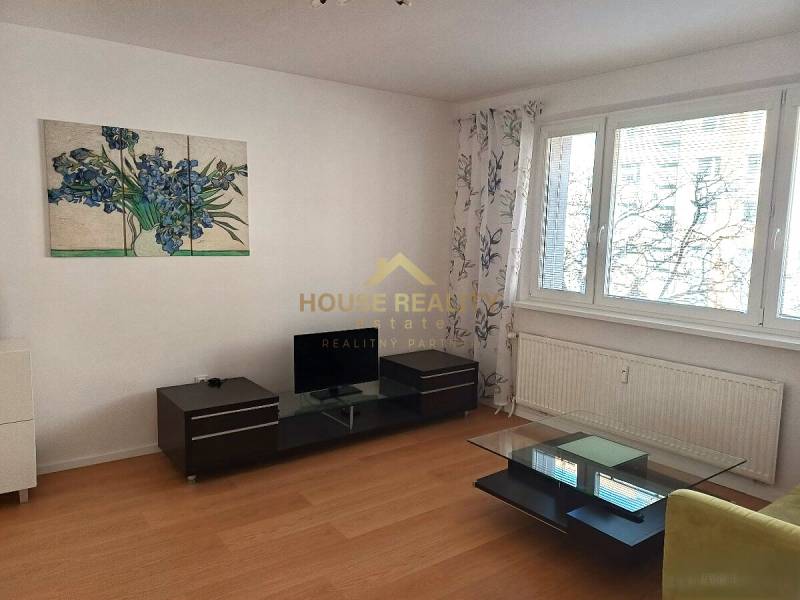 Nappali fa mintázatú padlóval, háromszobás lakásban, amely magában foglalja a televíziót és az asztalt.