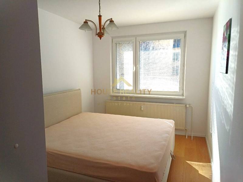 Hálószoba egy háromszobás lakásban, ággyal és fa dekorációjú padlóval.