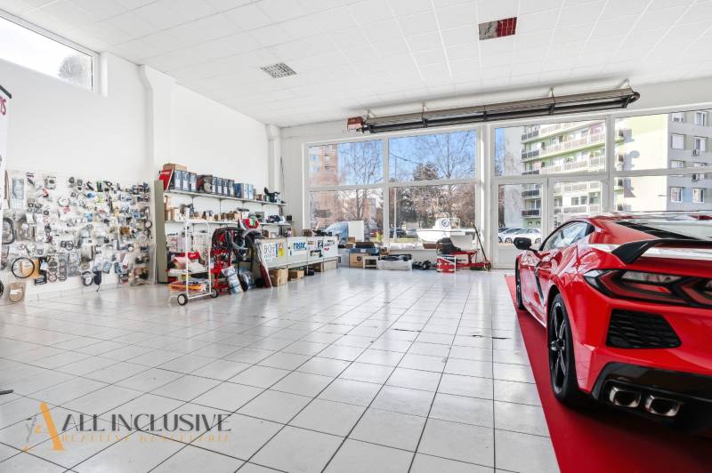 Autószerviz üzlethelyiség üveggel és kiállított autóval a burkolaton, alkatrészek a falakon.