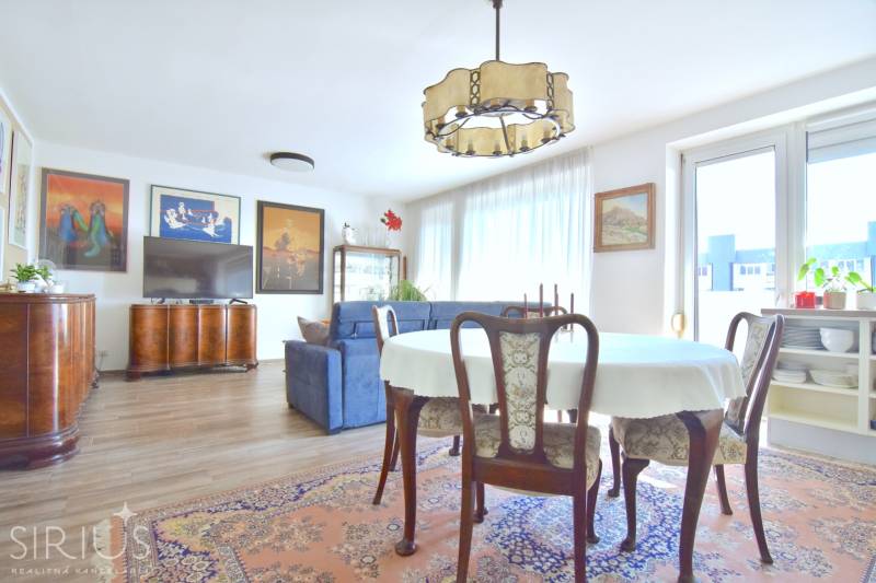 Nappali étkezőasztallal, kanapéval és fa dekorációjú padlóval egy háromszobás lakásban.