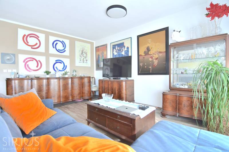 Nappali egy háromszobás lakásban fa bútorokkal, fa dekoros padlóval és képekkel a falakon.