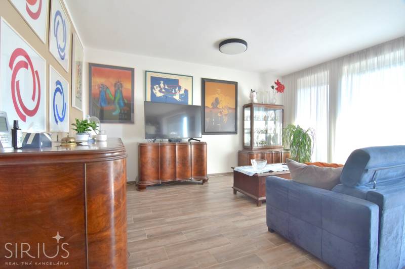 Nappali sötét bútorokkal, fa dekoros padlóval és dekoratív képekkel egy háromszobás lakásban.