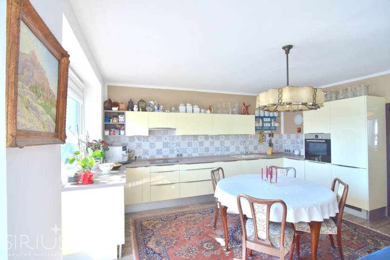 Konyha egy háromszobás lakásban fa bútorokkal, virágokkal és mintás szőnyeggel.