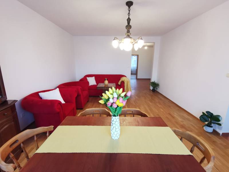 4 szobás lakás piros ülőgarnitúrával, étkezőasztallal és fa dekorációjú padlóval.