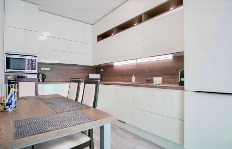 Konyha egy háromszobás lakásban fényes szekrényekkel és fa dekorációjú falakkal.