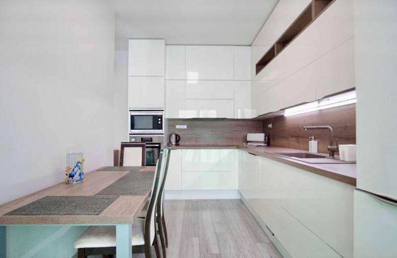 Konyha egy háromszobás lakásban, fa dekorációjú padlóval és világos bútorokkal.