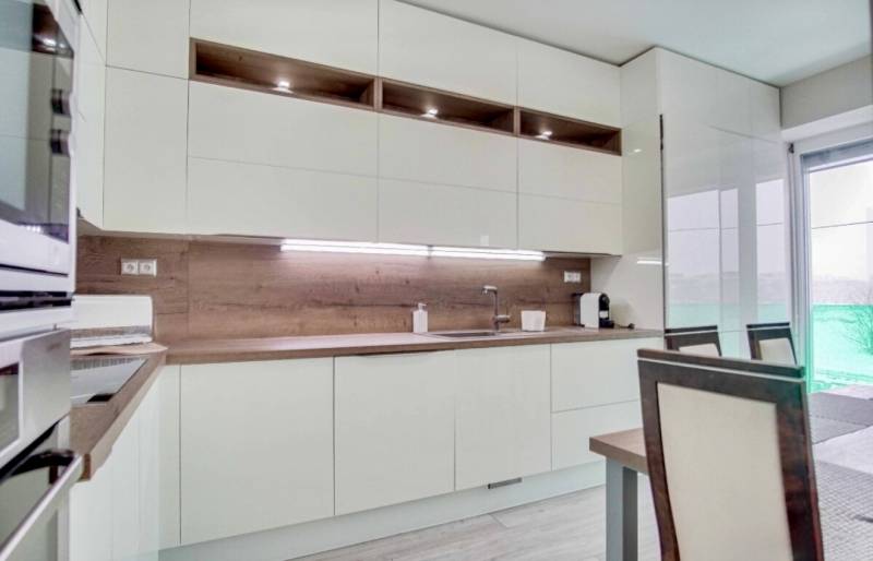 Konyha egy háromszobás lakásban fehér bútorokkal és fa mintájú padlóval.