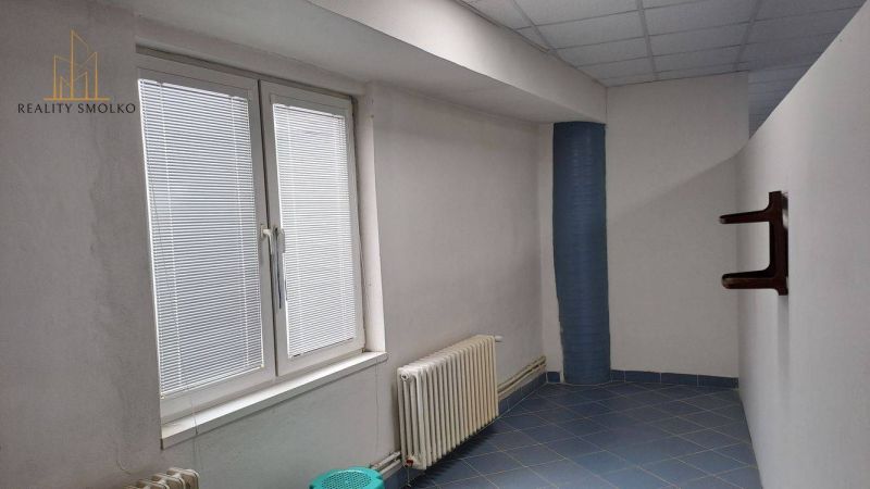 Üzlethelyiség belső tere csempézett padlóval, radiátorral és nagy ablakkal.