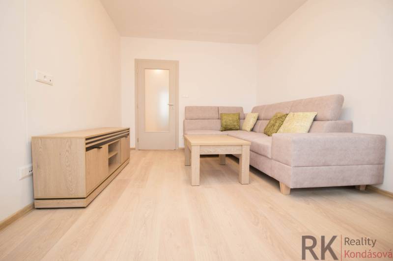 Nappali egy háromszobás lakásban kanapéval és fa mintázatú padlóval.