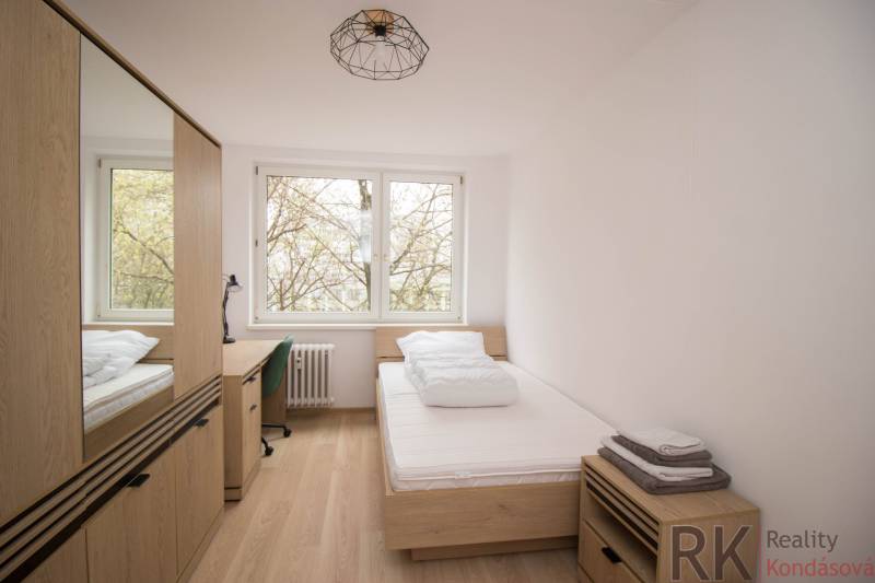 Szoba egy háromszobás lakásban ággyal, asztallal és fa dekorációjú padlóval.