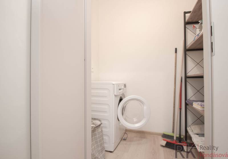 Mosókonyha egy háromszobás lakásban mosógéppel, polccal és tisztítószerekkel.