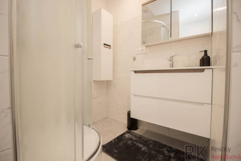 Fürdőszoba egy háromszobás lakásban, modern zuhanyzóval és fehér bútorokkal.