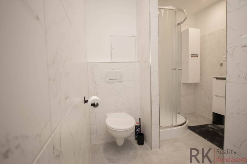 Fürdőszoba zuhanyzóval, WC-vel és fehér csempékkel egy háromszobás lakásban.