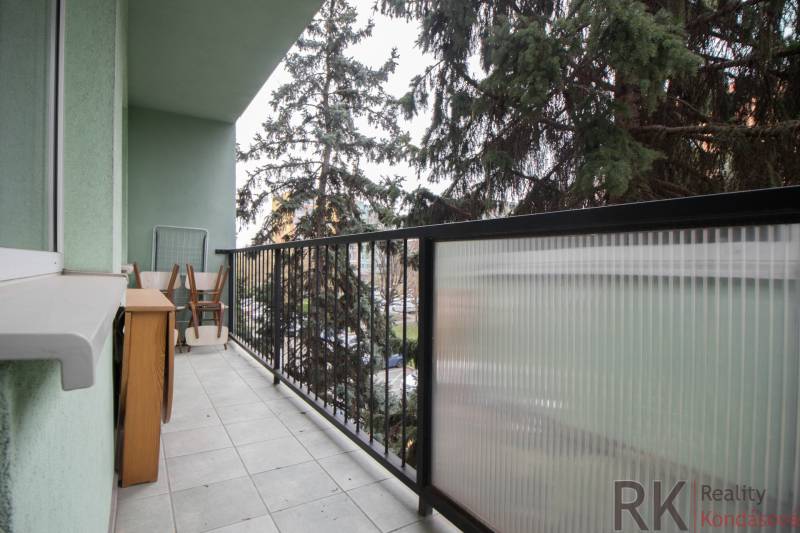 Erkély egy 3 szobás lakásban bútorokkal és korláttal, kilátással a zöldre.