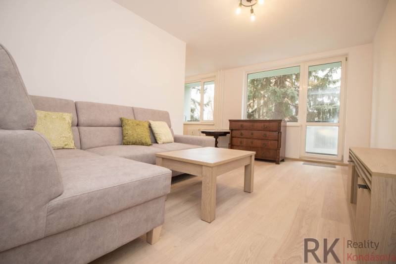 Nappali kanapéval, asztallal és fa dekor padlóval egy háromszobás lakásban.