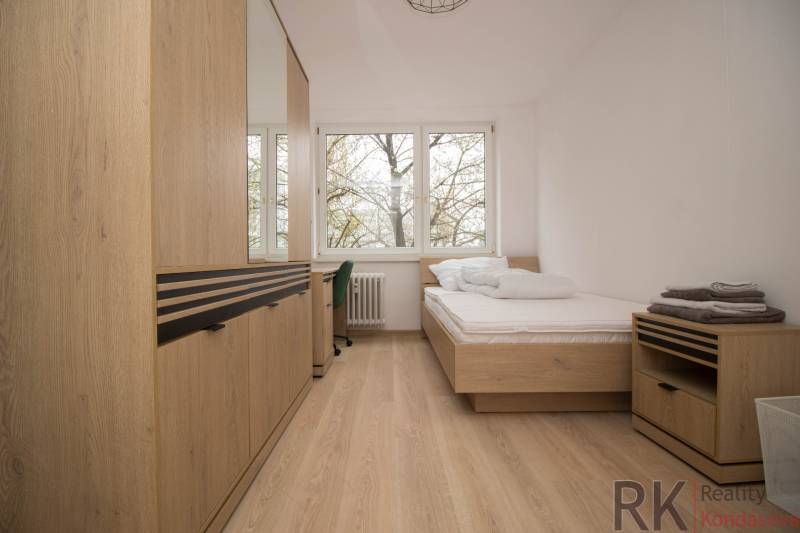 Világos hálószoba egy háromszobás lakásban, fa dekorációs padlóval és nagy ablakokkal.