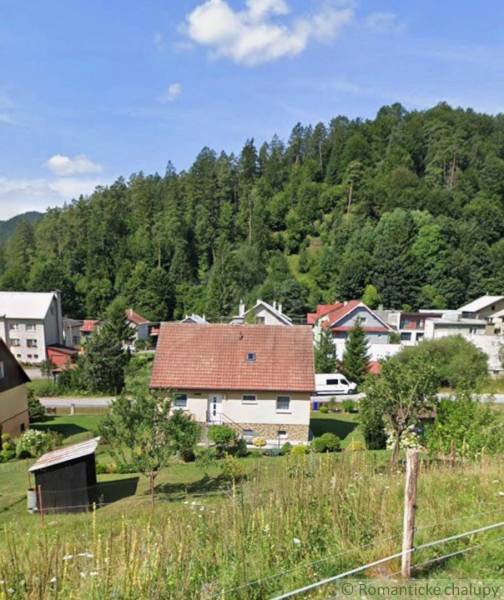 Családi ház Liptovské Revúcéban, zölddel körülvéve és további házakkal az erdő hátterében.