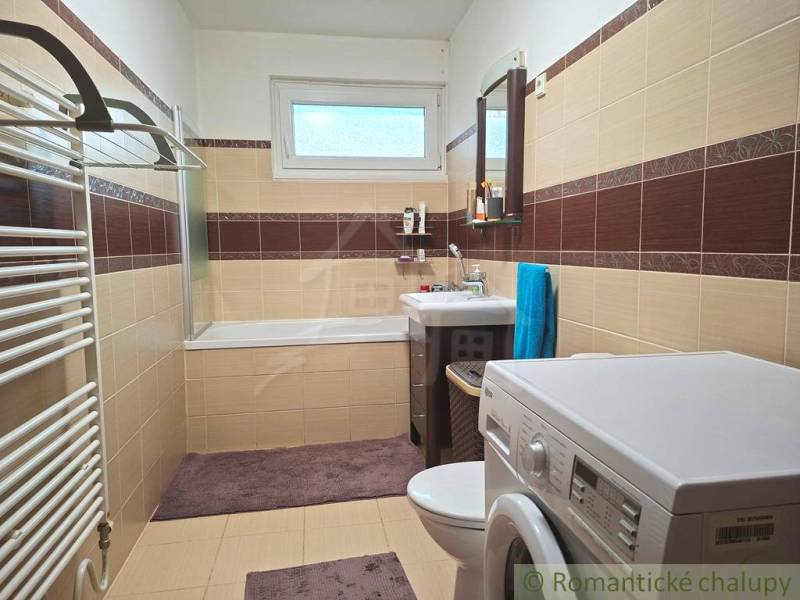 Családi ház fürdőszobája káddal, mosógéppel és barna-bézs csempével.