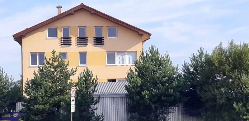 Sárga ház ferde tetővel és ablakokkal a fák mögött, közel az irodai vonalakhoz.