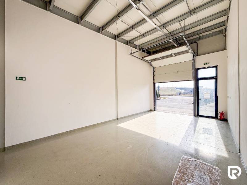 Kereskedelmi helyiségek nagy garázskapuval és szürke padlóval, világítással.