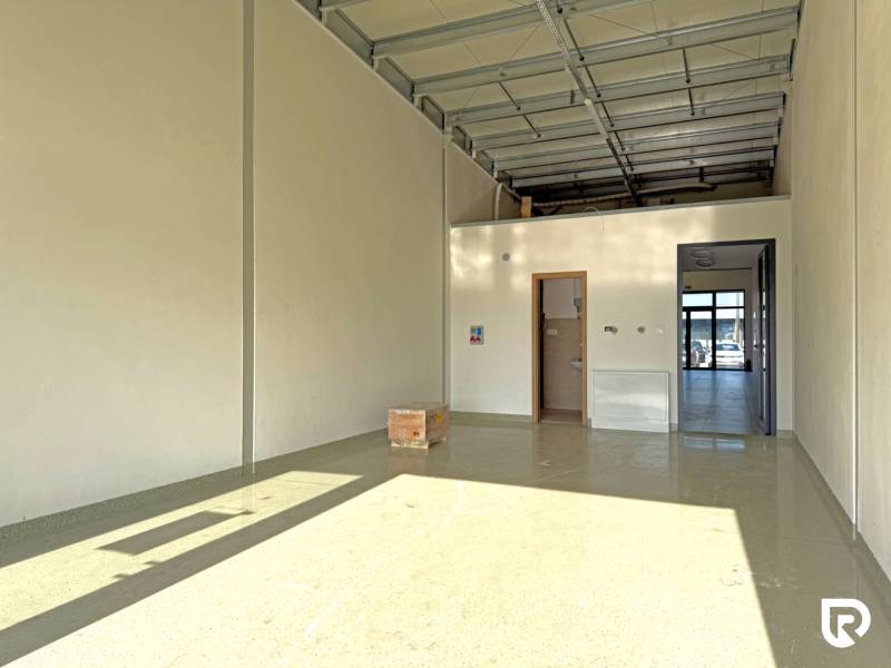 Tágas üzlethelyiség magas mennyezettel és betonpadlóval.