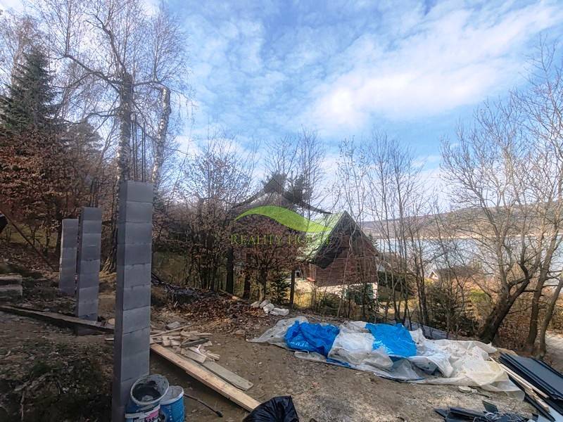 Építőanyag a Zajačia debra melletti házikó mellett Holčíkovce-ben, kilátással a vízfelületre.