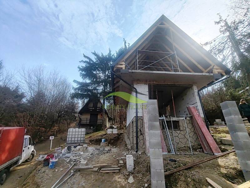 Nyúl-völgyi házikó építése Holčíkovce-ban, fákkal és építőanyaggal körülvéve.