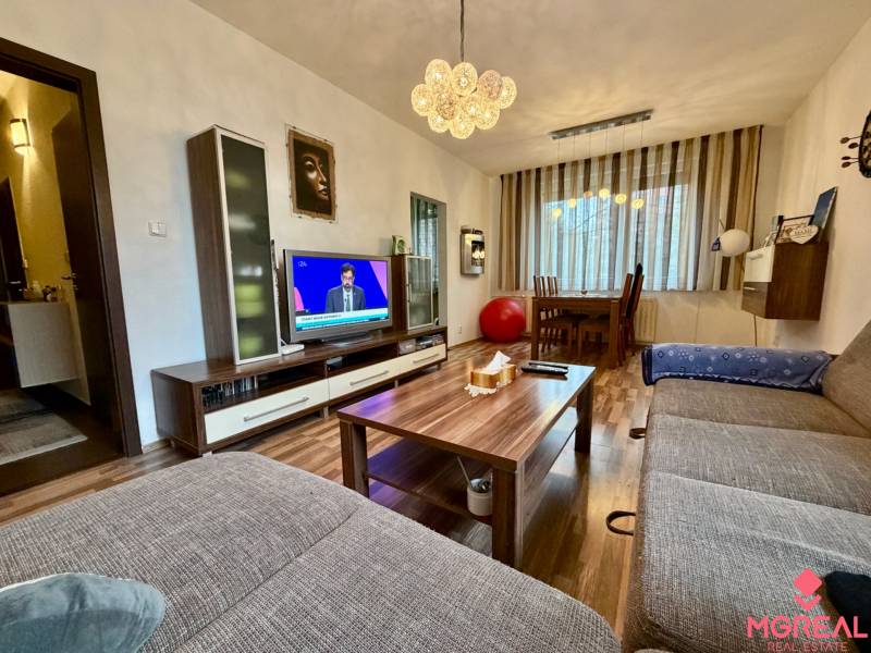 Nappali egy háromszobás lakásban, fa mintázatú padlóval és kényelmes kanapéval.