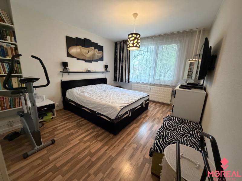 Hálószoba egy háromszobás lakásban fa mintázatú padlóval és szobakerékpárral.