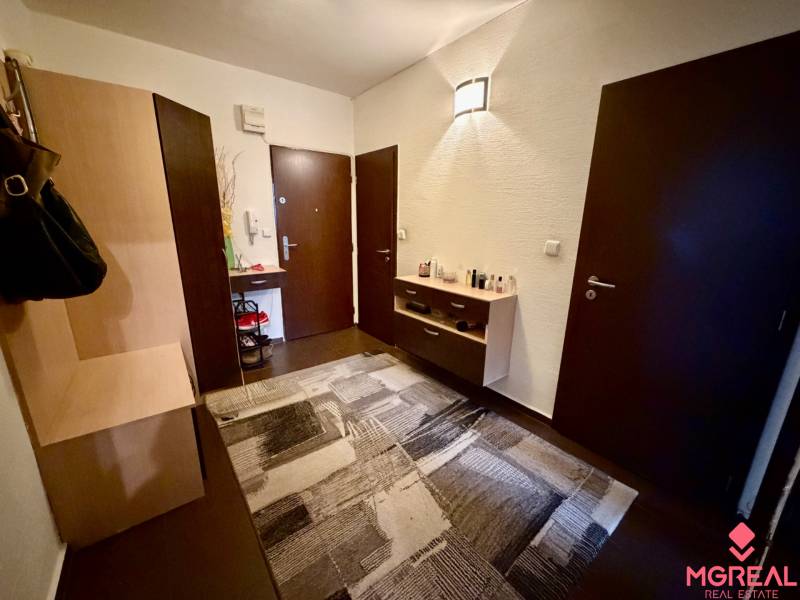 Előszoba sötét ajtókkal, komóddal és fa dekorációs padlóval egy háromszobás lakásban.