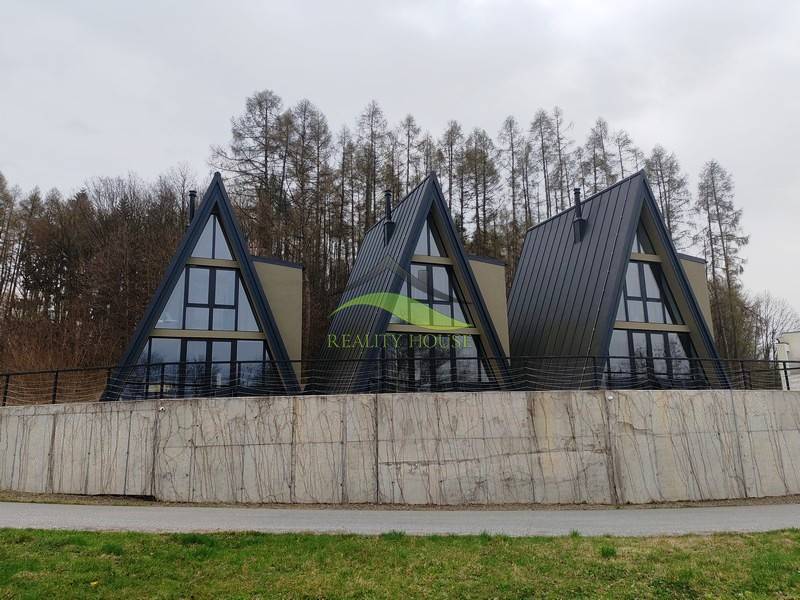 Háromszögletű tetővel rendelkező házak az Evy utcában, Holčíkovce településen, természet és erdő által körülvéve.