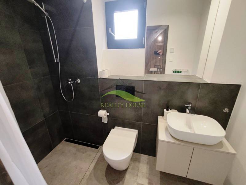 Fürdőszoba a házikóban zuhanyzóval, modern mosdókagylóval és WC-vel, fa dekorációjú padlón.