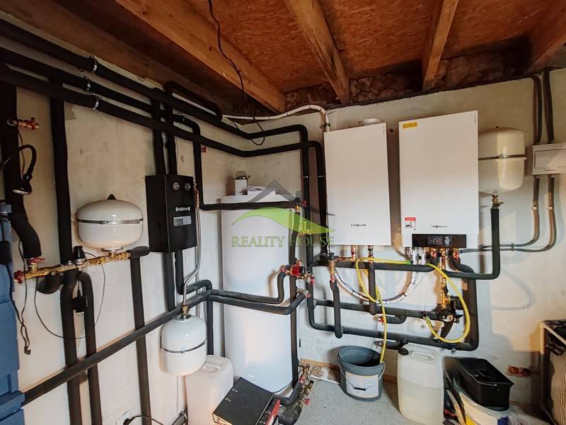 Fűtési technikai berendezés családi házban összekapcsolt csövekkel és bojlerrel.