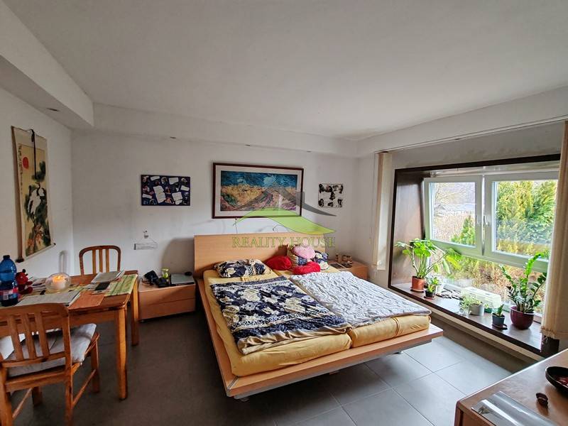 Hálószoba családi házban asztallal és nagy ablakkal, növények a párkányon.